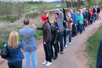 Ökumenischer Kreuzweg der Jugend Jugendliche stehen entlang eines Wanderweges hintereinander und reichen über die Köpfe hinweg ein lebensgroßes Kreuz weiter