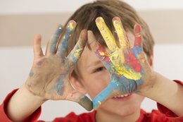 Ein Kleiner Junge streckt dem Betrachter bunt bemalte Hände entgegen